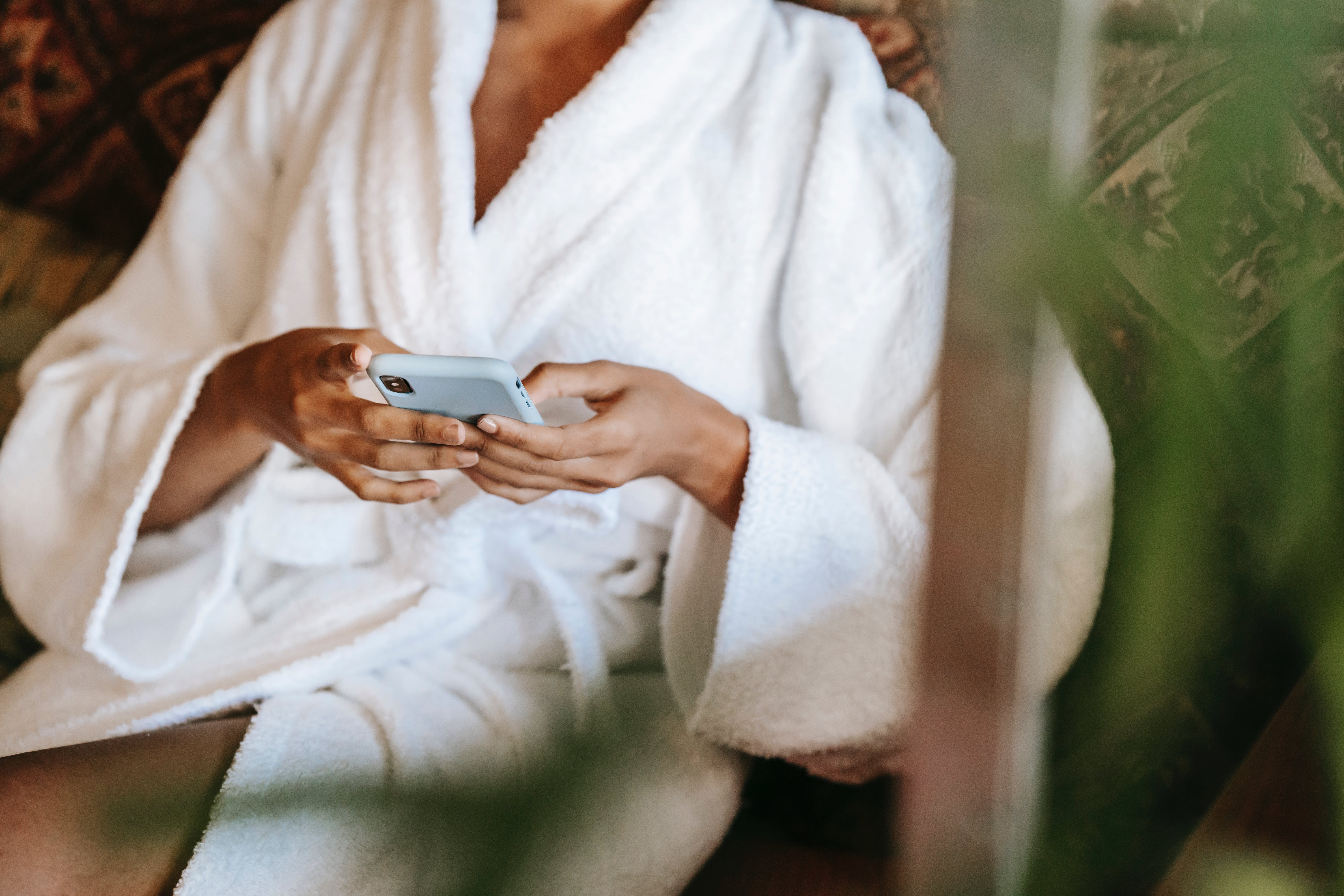 A serene scene of a client in a white robe, sitting in a relaxed pose and using a smartphone, possibly to book an appointment or inquire about services